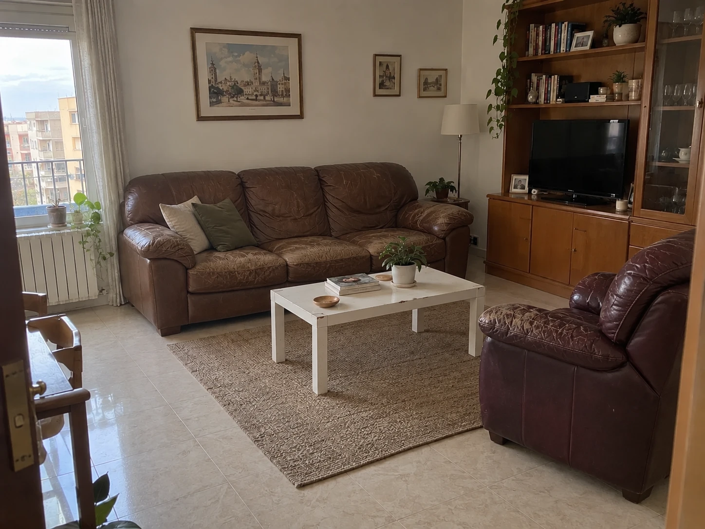 La misma habitación con sofá de cuero desgastado, butaca antigua y mesa de centro blanca sencilla